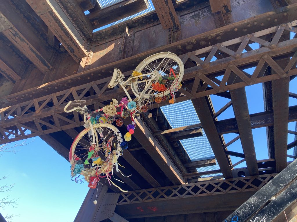 A white bike suspended from a brace on the underside of the railroad trestle.